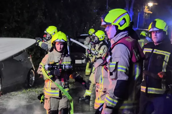 Mehrere Feuerwehrleute in gelben Helmen und Schutzkleidung halten Löschschläuche bei einem nächtlichen Einsatz.