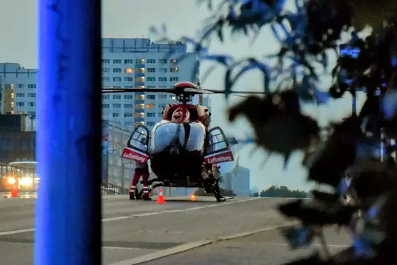 Rettungshubschrauber mit geöffneten Türen steht auf Straße, im Hintergrund Hochhaus und Bäume im Dämmerlicht.