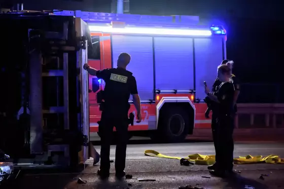 Zwei Polizisten stehen neben einem auf der Seite liegenden Fahrzeug, im Hintergrund ein beleuchtetes Feuerwehrfahrzeug.