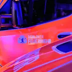 Nahaufnahme der Fahrertür eines orange-roten Fahrzeugs mit dem Schriftzug 'Berliner Feuerwehr' und einem Wappen.