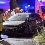 Schwarzer Hyundai mit beschädigter Front und Fahrerseite steht nachts auf Straße, Feuerwehrleute und Rettungskräfte umgeben das Fahrzeug.