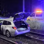 Silberner Kombi mit offener Heckklappe und geöffneter Fahrertür steht auf Bahngleisen, im Hintergrund weißes Fahrzeug mit gelbem Schriftzug 'Betriebsaufsicht' und Blaulicht.