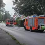 Zwei orangefarbene Feuerwehrfahrzeuge, eine Drehleiter und ein Lösch- und Hilfeleistungsfahrzeug, stehen auf einer Straße in einem Wohngebiet.
