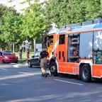 Feuerwehrfahrzeug mit geöffneten Seitenfächern steht auf Straße, Feuerwehrmann läuft daneben, mehrere Autos und Bäume im Hintergrund.