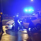 Mehrere Feuerwehrleute in Schutzkleidung, darunter zwei Polizisten, stehen bei einem beschädigten Renault auf nasser Straße bei Nacht, der Renault hat geöffnete Türen.