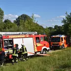 Zwei Feuerwehrfahrzeuge stehen auf einer Wiese, rechts Berliner Feuerwehr, links freiwillige Feuerwehr Ahrensfelde. Mehrere Feuerwehrleute in Schutzkleidung arbeiten am linken Fahrzeug.