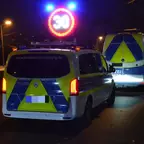 Zwei Polizeifahrzeuge mit reflektierenden Warnmarkierungen stehen nachts auf einer Straße, darüber leuchtet ein rundes, rotes Verkehrsschild mit der Zahl 30.