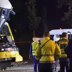 Mehrere Personen in Warnwesten und Polizeiuniform stehen nachts vor einer beschädigten gelben Straßenbahn und einem weißen Fahrzeug.