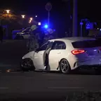 Weißer Pkw mit offener Fahrertür steht nachts auf der Straße, mehrere Feuerwehrleute in Schutzkleidung sind in der Nähe, Blaulicht im Hintergrund.