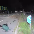 Nächtliche Unfallstelle auf einer Straße mit Trümmern und einem umgestürzten Verkehrszeichen, im Hintergrund ein Transporter und Einsatzkräfte.