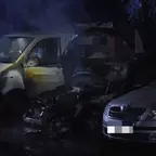 Drei geparkte, beschädigte Fahrzeuge bei Nacht, eines davon mit stark beschädigter Motorhaube und Rauchentwicklung.