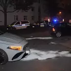 Zwei beschädigte Autos stehen nachts auf einer Straße, im Hintergrund sind Polizeifahrzeuge mit Blaulicht und mehrere Personen zu sehen.