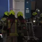 Mehrere Feuerwehrleute mit gelben Helmen und Schutzkleidung stehen vor einem Gebäude mit blauer Tür und Hausnummer 125.