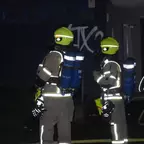 Zwei Feuerwehrleute in Schutzanzügen und gelben Helmen stehen nachts vor einem Gebäude mit Graffiti.