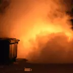 Große Rauchwolke neben einem Müllcontainer in der Nacht, davor liegt ein kleiner Karton auf dem Boden.