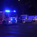 Feuerwehrfahrzeug mit eingeschaltetem Blaulicht steht neben einem Auto, das im Gleisbett steht, bei Nacht auf einer Straße mit Laterne.
