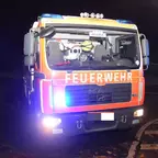 Feuerwehr-Löschfahrzeug mit eingeschaltetem Blaulicht steht nachts auf einer Straße.
