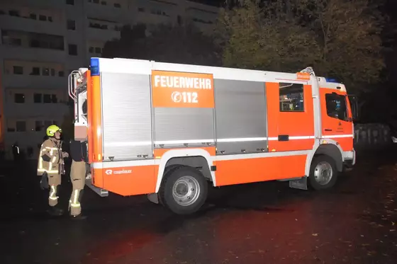 Tanklöschfahrzeug der Feuerwehr mit zwei Feuerwehrleuten in Schutzkleidung daneben, aufgenommen bei Nacht.