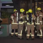 Gruppe von Feuerwehrleuten in Schutzkleidung und Helmen steht nachts vor einem Gebäude und bespricht sich.
