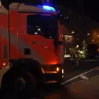 Feuerwehrauto mit Blaulicht steht an einer Haltestelle, mehrere Feuerwehrleute arbeiten an einem Fahrzeug im Hintergrund.