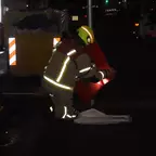Ein Feuerwehrmann kniet auf dunklem Boden und verpackt einen roten Rauchschutzvorhang, er trägt eine reflektierende Schutzkleidung und einen gelben Helm.