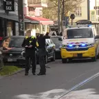 Zwei Polizisten stehen auf einem Bürgersteig neben parkenden Autos, ein Polizeifahrzeug, sowie ein Einsatzfahrzeug der BVG, mit Blaulicht steht auf der Straße.