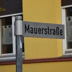 Straßenschild mit der Aufschrift 'Mauerstraße' vor einem gelb gestrichenen Haus mit zwei Fenstern.