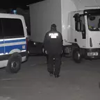 Polizist geht zwischen einem Polizeifahrzeug und einem LKW, der auf einem Parkplatz steht.