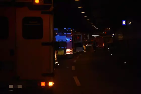 Mehrere Feuerwehrfahrzeuge stehen mit eingeschalteten Warnlichtern in einem dunklen Autobahntunnel auf der Fahrbahn.
