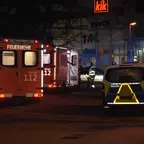 Feuerwehr- und Polizeifahrzeuge stehen nachts vor einem Einkaufszentrum mit Leuchtreklame.