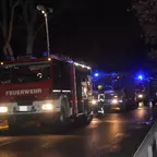 Mehrere Feuerwehrfahrzeuge mit eingeschalteten Blaulichtern stehen nachts auf einer Straße, Feuerwehrleute sind zu sehen.