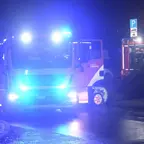 Feuerwehrfahrzeuge mit eingeschaltetem Blaulicht stehen nachts auf einer Straße, ein Fahrzeug hat geöffnete Türen.