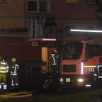Feuerwehrleute in Schutzkleidung stehen nachts vor einer Feuerwehrdrehleiter und leuchtendem Lichtbalken.