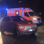 Rotes Mercedes-SUV steht nachts auf nasser Straße, im Hintergrund leuchtet ein Rettungswagen mit Blaulicht.