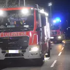 Zwei Feuerwehrfahrzeuge mit eingeschaltetem Blaulicht stehen nachts auf einer Straße.