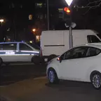 Ein weißer PKW steht auf einem Gehweg an einer Ampel, im Hintergrund ein weißer Transporter und ein Polizeifahrzeug mit Blaulicht bei Dunkelheit.
