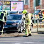 Drei Feuerwehrleute in Schutzkleidung entfernen ein Metallgeländer vor einem schwarzen VW-PKW in einer Haltestelle.