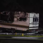 Ausgebrannter Wohnwagen mit stark beschädigtem Dach und Seitenwänden, nachts aufgenommen, Schläuche liegen davor.