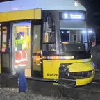 Straßenbahn mit beschädigter Front und geöffneten Türen, daneben zwei Personen in Warnwesten und ein Polizist bei Nacht