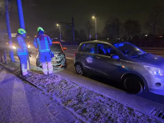 Zwei Einsatzkräfte in Schutzkleidung stehen neben einem beschädigten Auto am Straßenrand, ein weiteres Auto steht davor, nachts auf einer Straße mit Straßenlaternen