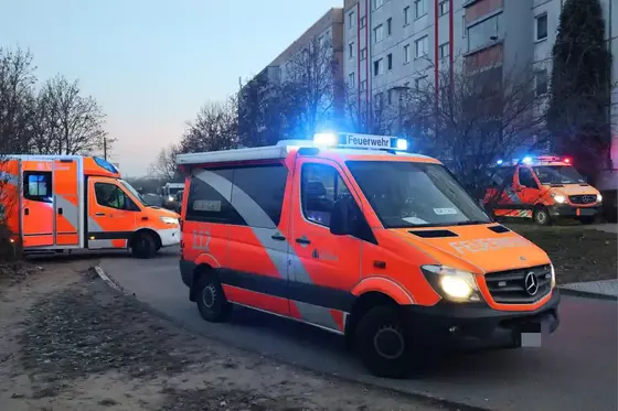 Mehrere Feuerwehrfahrzeuge mit Blaulicht stehen vor einem mehrstöckigen Wohnhaus in einer Wohnsiedlung