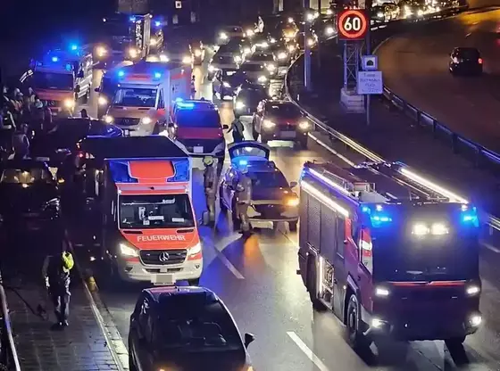 Nächtliche Autobahnszene mit Feuerwehr- und Polizeifahrzeugen mit Blaulicht, mehreren stehenden Autos und Einsatzkräften auf der Fahrbahn bei einem Verkehrsunfall