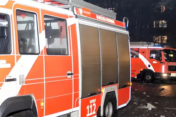 Zwei orange-weiße Feuerwehrfahrzeuge mit geschlossenen Fächern stehen nachts auf einer Straße