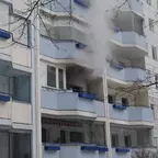 Rauch steigt aus einem Fenster eines mehrstöckigen Wohnhauses mit blauen Balkongeländern.