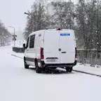 Weißer Polizeiwagen steht bei Schneetreiben auf einer schneebedeckten Straße auf einer Brücke mit Metallgeländer.