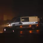 Silbener Einsatzwagen der Wasserschutzpolizei bei Nacht mit eingeschaltetem Licht auf nasser Straße, bei Nebel.