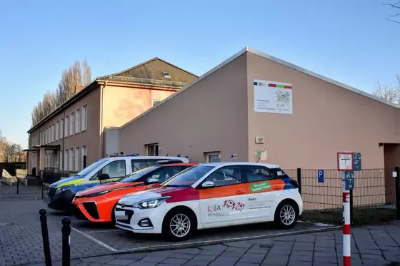 Drei Fahrzeuge mit Werbeaufschriften stehen vor einem hellen Gebäude mit einem Schild an der Fassade