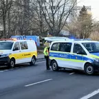 Polizeifahrzeug und gelber Einsatzwagen stehen auf einer Straße, daneben steht eine Person in Warnweste