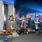 Feuerwehrleute in Schutzkleidung und Atemschutz löschen einen Brand an einem Gebäude in der Nacht mit einem Löschschlauch