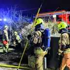 Feuerwehrleute in Schutzkleidung und Helmen stehen nachts mit Atemschutzgeräten und einem Einreißhaken vor einem Feuerwehrauto mit Blaulicht